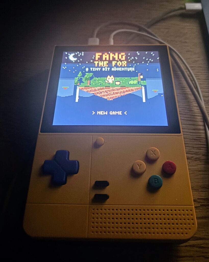 A Retroid Pocket on a desk at night, showing Fang the Fox's title screen: Fang on a floating island under the moon